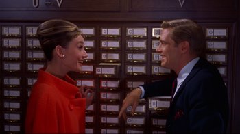 Movie still from “Breakfast at Tiffany's” (1961), directed by Blake Edwards – A man and a woman talking in front of each other in front of a card catalog; Medium shot, Low angle