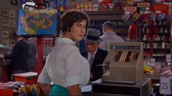 Movie still from “Breakfast at Tiffany's” (1961), directed by Blake Edwards – A woman standing in front of a cash register in a store; Medium shot, Over the shoulder angle
