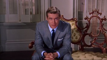 Movie still from “Breakfast at Tiffany's” (1961), directed by Blake Edwards – A man in a suit and tie sitting on a chair; Medium shot, Over the shoulder angle