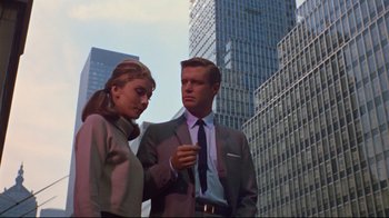 Movie still from “Breakfast at Tiffany's” (1961), directed by Blake Edwards – A man and a woman standing next to each other in front of some buildings; Medium shot, Low angle