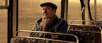 An older man sitting on a bus in the rain