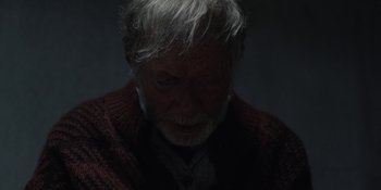 Movie still from “Dark” (2017), created by Baran bo Odar – An old man with a gray beard wearing a red sweater; Close Up shot, Overhead angle