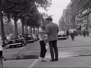 Movie still from “Breathless” (1960), directed by Jean-Luc Godard – A man and a woman standing on the side of the street; Wide shot, Over the shoulder angle