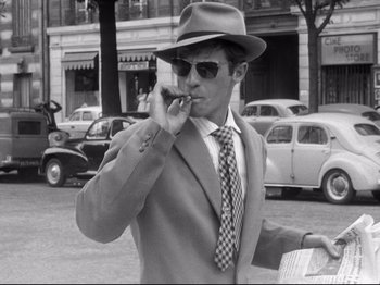Movie still from “Breathless” (1960), directed by Jean-Luc Godard – A black and white photo of a man smoking a cigarette; Medium shot, High angle