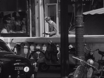 Movie still from “Breathless” (1960), directed by Jean-Luc Godard – A man in a hat is standing on a balcony; Wide shot, High angle