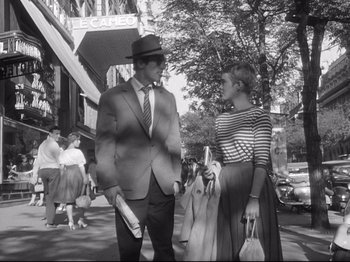 Movie still from “Breathless” (1960), directed by Jean-Luc Godard – A man and a woman standing on the sidewalk; Wide shot, Low angle