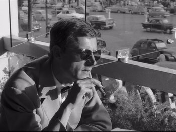 Movie still from “Breathless” (1960), directed by Jean-Luc Godard – A black and white photo of a man wearing a suit and tie; Medium shot, Low angle
