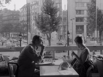 Movie still from “Breathless” (1960), directed by Jean-Luc Godard – A man and a woman sitting at a table in front of a window; Medium shot, High angle