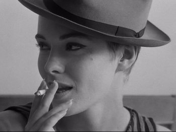 Movie still from “Breathless” (1960), directed by Jean-Luc Godard – A person wearing a hat smoking a cigarette; Close Up shot, Over the shoulder angle
