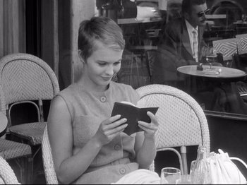 Movie still from “Breathless” (1960), directed by Jean-Luc Godard – A woman sitting at an outdoor cafe looking at a book; Medium shot, High angle