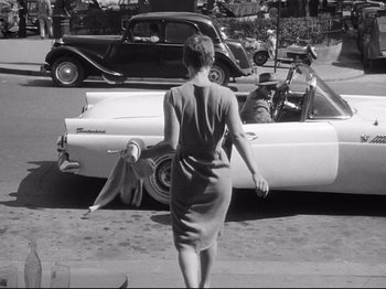 Movie still from “Breathless” (1960), directed by Jean-Luc Godard – A woman walking down the street in front of an old car; Wide shot, Low angle