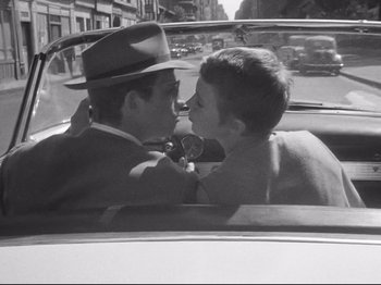 Movie still from “Breathless” (1960), directed by Jean-Luc Godard – A man and a woman kissing in a car on the street; Close Up shot, High angle