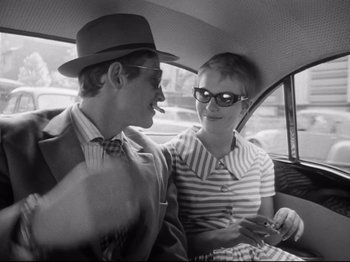 Movie still from “Breathless” (1960), directed by Jean-Luc Godard – A man and a woman sitting in the back of a car; Medium shot, Over the shoulder angle