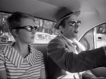Movie still from “Breathless” (1960), directed by Jean-Luc Godard – A man and a woman sitting in the back of a car; Medium shot, Low angle
