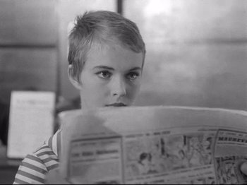 Movie still from “Breathless” (1960), directed by Jean-Luc Godard – A young boy reading a newspaper in black and white; Close Up shot, Over the shoulder angle