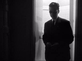 Movie still from “Breathless” (1960), directed by Jean-Luc Godard – A black and white photo of a man in a suit and tie; Medium shot, Low angle