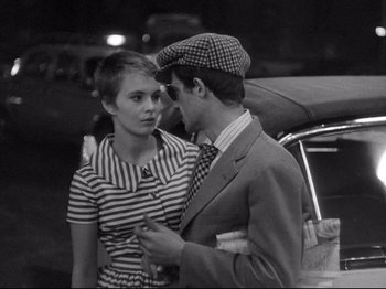 Movie still from “Breathless” (1960), directed by Jean-Luc Godard – A man and a woman standing next to each other in front of a car; Medium shot, Over the shoulder angle