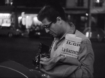 Movie still from “Breathless” (1960), directed by Jean-Luc Godard – A man is holding a guitar while standing next to a car; Close Up shot, Low angle