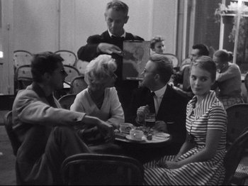 Movie still from “Breathless” (1960), directed by Jean-Luc Godard – A group of people sitting around a table; Medium shot, Over the shoulder angle