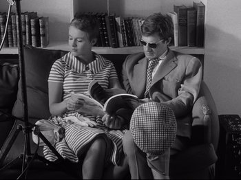 Movie still from “Breathless” (1960), directed by Jean-Luc Godard – A man and a woman sitting on a couch reading; Medium shot, High angle