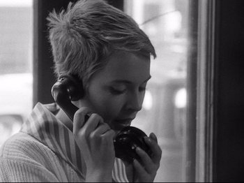 Movie still from “Breathless” (1960), directed by Jean-Luc Godard – A person holding a phone to their ear and eating a donut; Close Up shot, High angle
