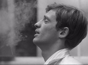 Movie still from “Breathless” (1960), directed by Jean-Luc Godard – A young man is smoking a cigarette in a black and white photo; Close Up shot, Low angle