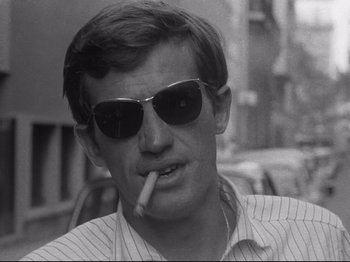 Movie still from “Breathless” (1960), directed by Jean-Luc Godard – A black and white photo of a man smoking a cigarette; Close Up shot, Low angle