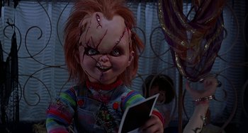Movie still from “Bride of Chucky” (1998), directed by Ronny Yu – A chucky doll holding a book in front of a mirror; Medium shot, Low angle