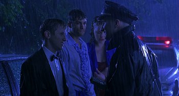 Movie still from “Bride of Chucky” (1998), directed by Ronny Yu – A group of people standing in the rain next to each other; Medium shot, Over the shoulder angle