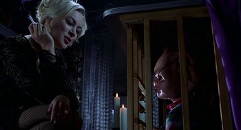 Movie still from “Bride of Chucky” (1998), directed by Ronny Yu – A woman standing next to a doll in a room with lit candles; Medium shot, Low angle