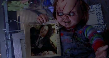 Movie still from “Bride of Chucky” (1998), directed by Ronny Yu – A creepy doll holding up a newspaper with a picture of a child; Medium shot, Over the shoulder angle