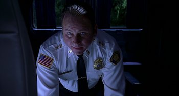 Movie still from “Bride of Chucky” (1998), directed by Ronny Yu – A man in a police uniform sitting on a chair; Close Up shot, Low angle