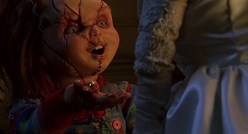 Movie still from “Bride of Chucky” (1998), directed by Ronny Yu – A creepy doll with blood all over its face; Close Up shot, Over the shoulder angle