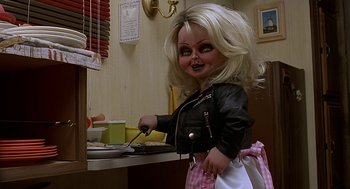 Movie still from “Bride of Chucky” (1998), directed by Ronny Yu – A creepy doll is cooking in a kitchen; Medium shot, Low angle