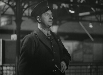 Movie still from “Brief Encounter” (1945), directed by David Lean – An older man in a military uniform is standing in a train station; Medium shot, Low angle