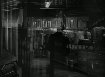 Movie still from “Brief Encounter” (1945), directed by David Lean – A man standing in front of a store at night; Wide shot, Over the shoulder angle