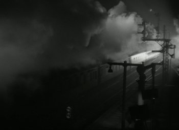 Movie still from “Brief Encounter” (1945), directed by David Lean – A train traveling down train tracks next to a train station; Extreme Wide shot, High angle