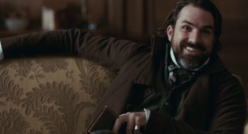 Movie still from “Bright Star” (2009), directed by Jane Campion – A man sitting on top of a couch holding a book; Medium shot, High angle