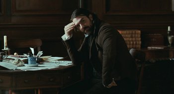 Movie still from “Bright Star” (2009), directed by Jane Campion – A man sitting in front of a desk with papers on it; Medium shot, High angle