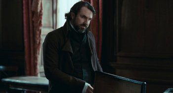 Movie still from “Bright Star” (2009), directed by Jane Campion – A man with a beard is standing in front of a desk; Medium shot, Over the shoulder angle