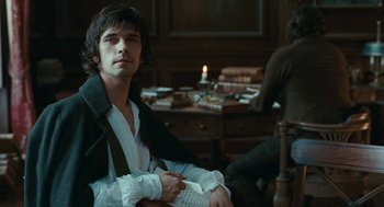 Movie still from “Bright Star” (2009), directed by Jane Campion – A man sitting in a chair in front of a table; Medium shot, Over the shoulder angle
