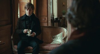 Movie still from “Bright Star” (2009), directed by Jane Campion – A man sitting on top of a couch holding a coffee cup; Medium shot, Over the shoulder angle