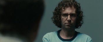 A man with curly brown hair and glasses stares at the camera