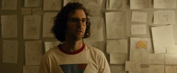 A man with curly hair wearing glasses and a t - shirt