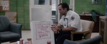 Movie still from “Bringing Out the Dead” (1999), directed by Martin Scorsese – A man sitting in front of a poster of a bird; Medium shot, Over the shoulder angle