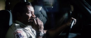 Movie still from “Bringing Out the Dead” (1999), directed by Martin Scorsese – A man with a watch is eating something while sitting in a car; Close Up shot, Low angle