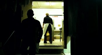 Movie still from “Bronson” (2008), directed by Nicolas Winding Refn – A man is walking into a kitchen with a towel; Wide shot, Low angle