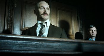Movie still from “Bronson” (2008), directed by Nicolas Winding Refn – A man in a suit sitting in front of a wooden wall; Close Up shot, Low angle