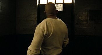 Movie still from “Bronson” (2008), directed by Nicolas Winding Refn – A man in a white shirt is looking out of a window; Medium shot, Low angle