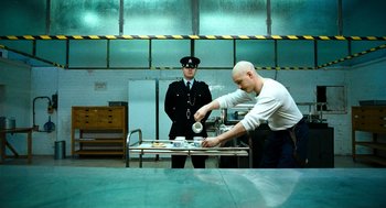 Movie still from “Bronson” (2008), directed by Nicolas Winding Refn – A man in a white shirt and a man in a black uniform; Medium shot, Over the shoulder angle